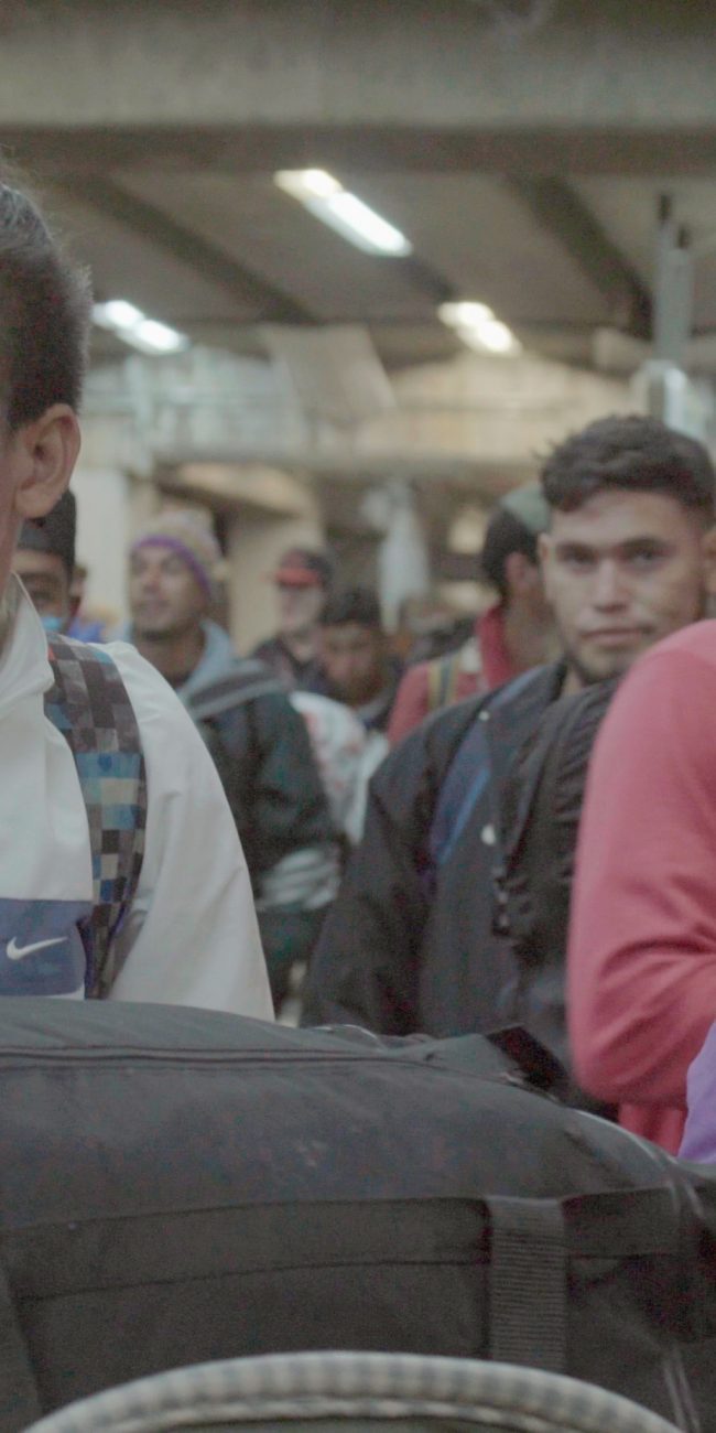 Mike y Yuri del documental La Caravana cargando sus bolsas entre muchos migrantes de la caravana