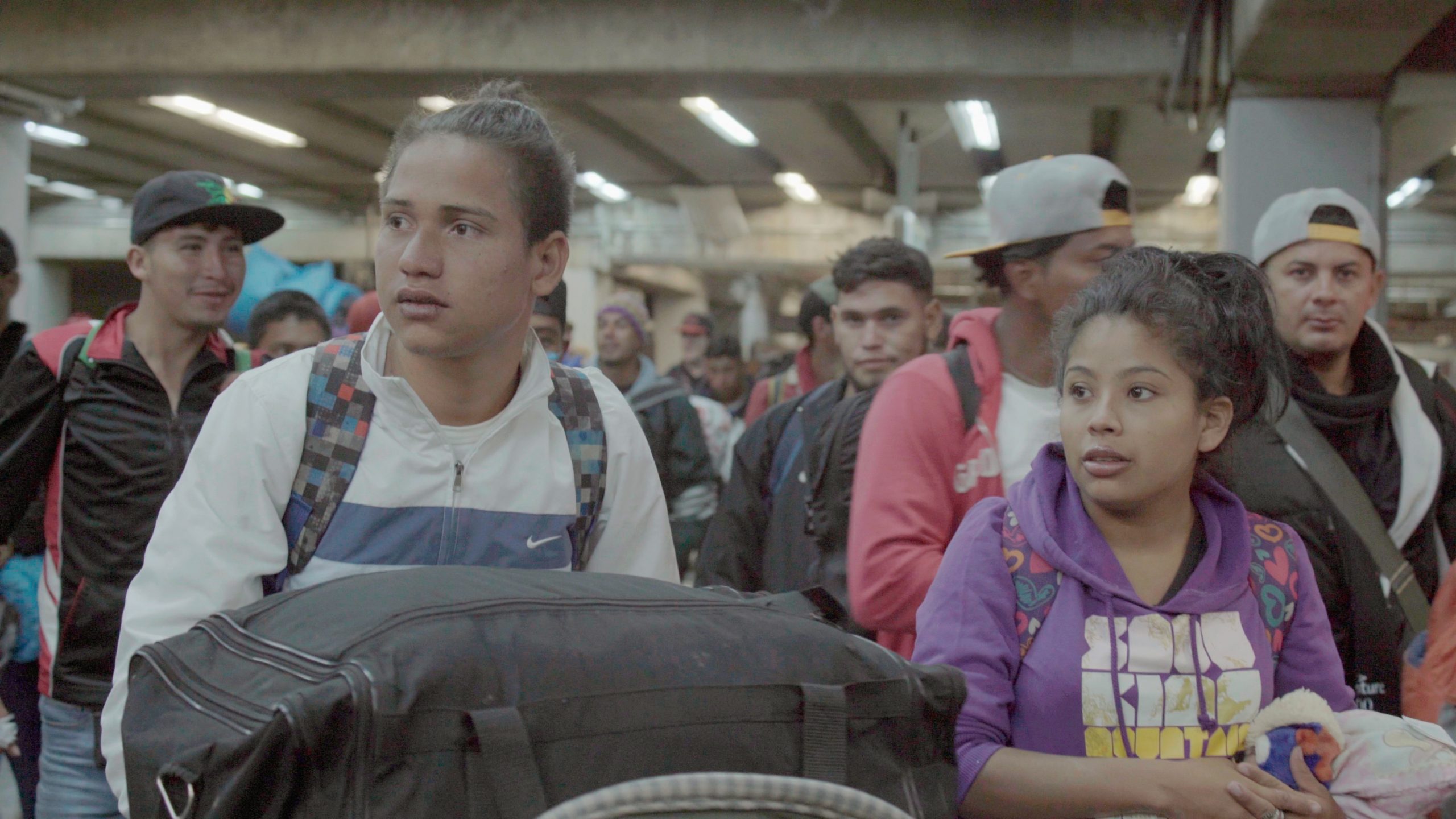 Mike y Yuri del documental La Caravana cargando sus bolsas entre muchos migrantes de la caravana
